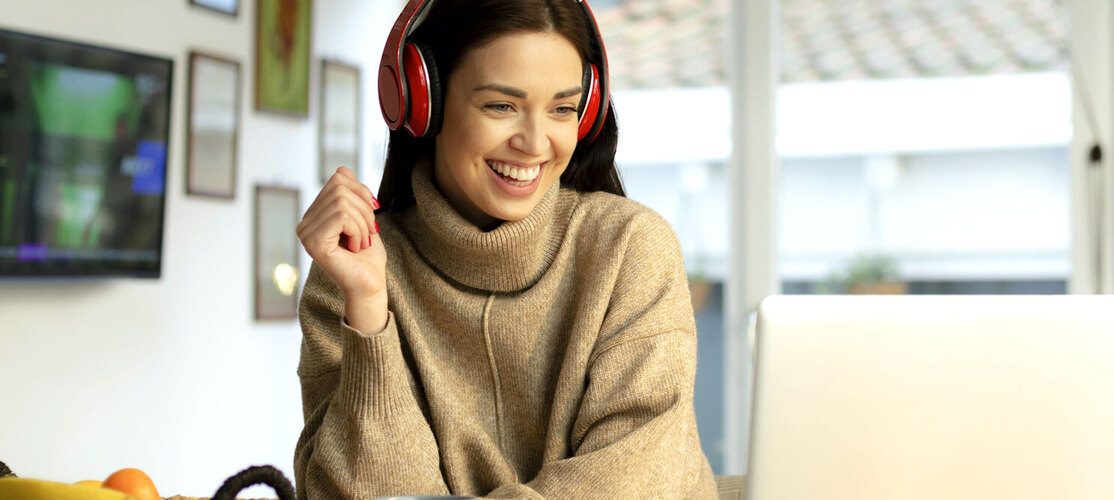 ragazza sorridente seduta davanti al pc con cuffie rosse