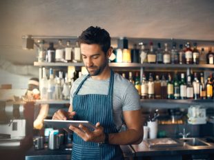 uomo con grembiule consulta tablet in un bar
